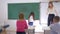 Schoolgirl writes an simple example on chalkboard near educator on math lesson, primary education