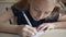 Schoolgirl writing by pen on checkered paper at table on lesson. Close up student girl writing word on checkered sheet