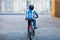 Schoolkid boy in safety helmet riding with bike in the city with backpack. Happy child in colorful clothes biking on