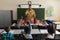 Schoolkids raising hands while male firefighter teaching about fire safety in classroom