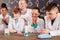 Schoolkids in whitecoats and protective eyeglasses watching chemical reactions