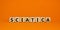 Sciatica symbol. Wooden cubes with word `sciatica`. Beautiful orange background. Medical and sciatica concept. Copy space