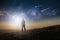 A science fiction concept. A man standing on a hill looking out across space with shooting stars in the sky