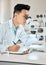 Science, writing and microscope with an asian man doctor working in a lab for research or innovation. Healthcare