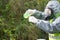 A scientist in a gray protective suit and mask, pours a green liquid from a flask into a test tube, against the background of