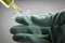 Scientist with green latex gloves manipulates vial and syringe in laboratory