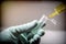 Scientist with green latex gloves manipulates vial and syringe in laboratory