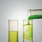 Scientist hand pouring a green chemical solution from a laboratory glass test tube into a scientific cylinder with yellow liquid f