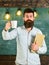 Scientist holds book and drinks coffee, chalkboard on background, copy space. Coffee break concept. Man with beard on