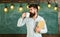 Scientist holds book and drinks coffee, chalkboard on background, copy space. Man with beard on calm face in classroom