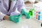 A scientist`s hand Wear green gloves Several colored chemicals are being tested in a test tube placed on a white table. To conduc