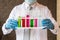 Scientist wear white dress and blue gloves holding multicolor glass test tube. Chemist examines chemical test tube,