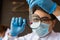 Scientist wear white dress and blue gloves uses a magnifying glass to see the glass test tube.