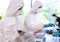 Scientists in protection suits and masks working in research lab using laboratory equipment: microscopes, test tubes.