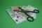 Scissors and euro banknotes over green background