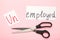 Scissors with word unemployed on pink background