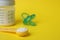 Scoop of powdered infant formula, feeding bottle and pacifier on yellow background, space for text. Baby milk