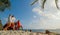 Scooter road trip. Lovely couple on red motorbike in white clothes on sand beach. People walking near the tropical palm