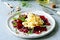 Scramble of eggs with carpaccio of baked beets with walnuts, aromatic herbs and arugula on a plate.