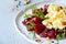 Scramble of eggs with carpaccio of baked beets with walnuts, aromatic herbs and arugula on a plate.