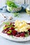 Scramble of eggs with carpaccio of baked beets with walnuts, aromatic herbs and arugula on a plate.