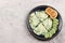 Scrambled eggs with green onions and cheese with toast and sliced cucumbers on a round plate on a light gray background