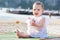 Screaming baby girl in white dress. Infant sitting on the sandy tropical beach