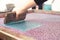 A screen printing squeegee is guided by hand over a silk-screen and shoves cyan paint over a detailed clover design