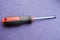 Screwdriver with rubberized red-black handle and black tip, cross-shaped slit