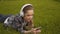 Scrolling, searching on the internet, a young woman lies on the grass in large headphones, and watches video on the