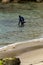 Scuba Diver Wearing a Wetsuit and Air Tank Stands Up in Shallow Ocean at End of Dive