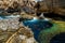 Scuba divers in wetsuits prepare to dive under water near a beautiful canyon