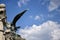 The sculptural image of a formidable eagle on an ancient colonade against blue sky with clouds. Turul Eagle Statue at main gate of