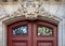 Sculptural volute and relief stone elements above top of old brown wooden door with glass windows. Antique ornate doorway arch.