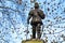 Sculpture against the clear blue sky surrounded by autumn trees with dark leaves withered