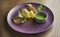 Sea bass fillet fried in olive oil with a side dish of creamy rice and green sauce on a purple ceramic plate on a wooden