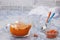 Sea buckthorn tea in a glass teapot, fresh sea buckthorn and two glass cups on a light blue marble background
