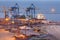 Sea commercial port at night in Mariupol, Ukraine. Industrial view. Cargo freight ship with working cranes bridge in sea port