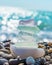 Sea glass stones arranged in a balance pyramid on the beach. Beautiful azure color sea with blurred seascape background.