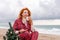 Sea Lady in plaid shirt with a mug in her hands enjoys beach with Christmas tree. Coastal area. Christmas, New Year