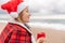 Sea Lady in Santa hat plaid shirt with a red mug in her hands enjoys beach with Christmas tree. Coastal area. Christmas