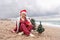 Sea Lady in Santa hat plaid shirt with a red mug in her hands enjoys beach with Christmas tree. Coastal area. Christmas