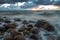 A sea landscape with rocks, a storm and a setting sun. Waves, rocks, storm and clouds.n