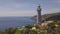 Sea lighthouse on green mountains and rocky shore drone view. Aerial view light house on mountain cliff and turquoise