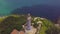 Sea lighthouse on mountain cliff and sailing ships drone view. Aerial landscape sea light house on green mountain and