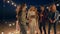 Sea party, group of friends dance and enjoy rest on sandy beach in lighting of lamps