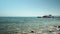 Sea pebble beach with moored red yacht near beach. Seashore with clear calm sea water and recreational facilities on beach. Summer