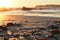 Sea, rocks, sandy beach with many shells in the sand. Sunset with golden highlights.