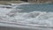 Sea rolling waves onto shore hitting them against ground and breaking into foam