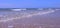 Sea shore with long big waves and pier in distance oin sand beach at sunny day.